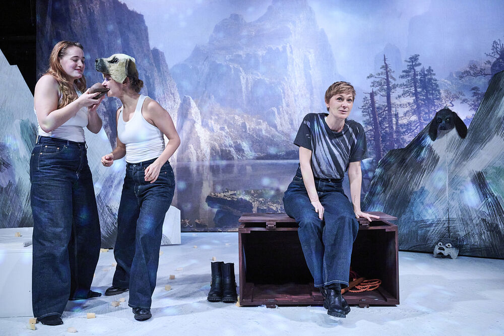 Drei Schauspielerinnen vor einer Berglandschaft. Eine sitzt, die anderen beiden stehen am Rand. 