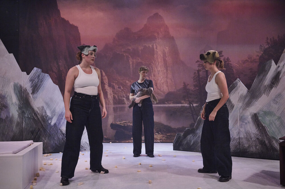 Drei Schauspielerinnen vor einer Berglandschaft. Zwei stehen sich drohend gegenüber, die dritte hält einen Hasen. 